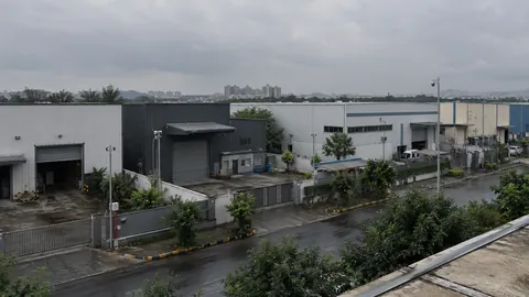 Low industrial units along a wet service road under a flat grey sky.