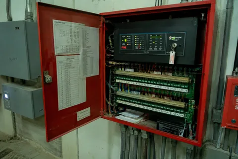 A fire alarm panel open in its red enclosure, the loop cards and field wiring exposed inside.