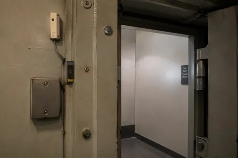 A heavy steel door part open in a bare corridor, the contact and its wiring visible on the frame.