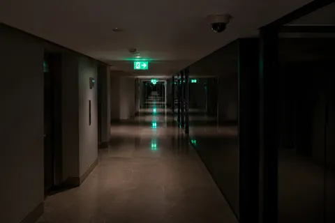 A corridor at night lit only by the green of the emergency exit signs along it.