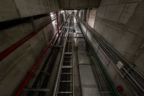 A lift shaft photographed from above, guide rails and cabling running down its full height.